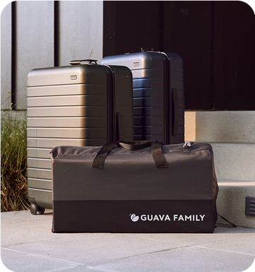 Guava's Lotus Travel Crib packed in carrier alongside a couple of suitcases